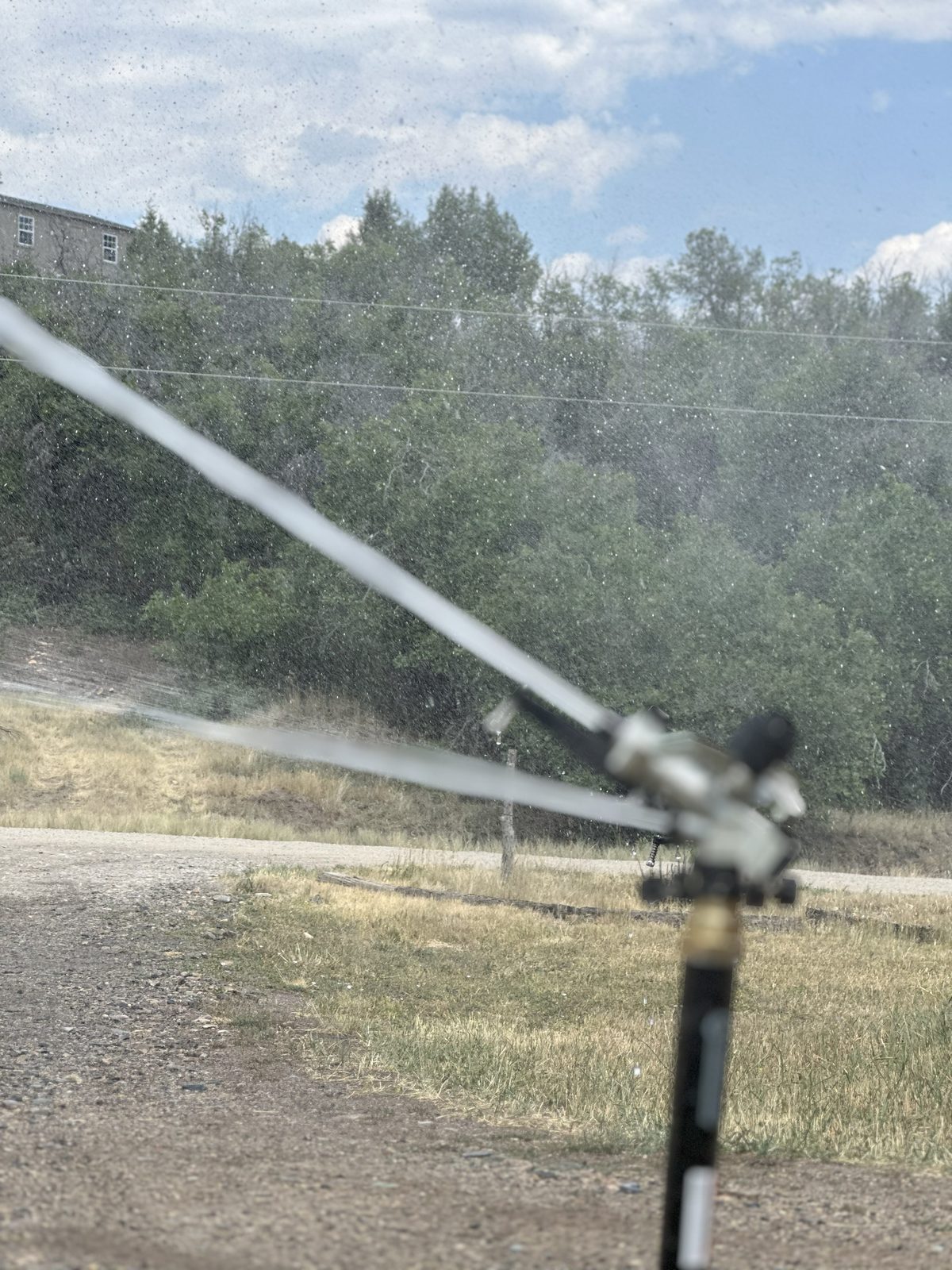Sprinkler firing water arc over log pile — defensible space pre-wetting